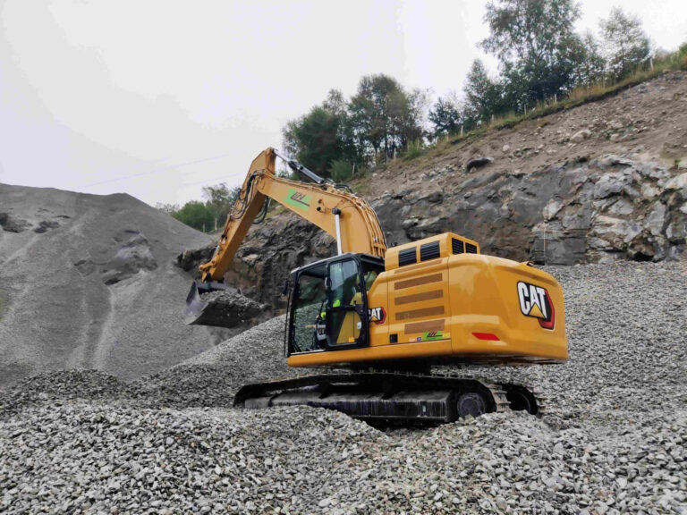 Yellow CAT excavator working in a gravel quarry, arm extended to scoop rocks from a pile.