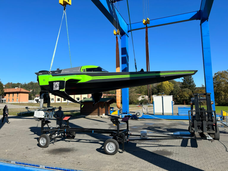 Green and black racing powerboat suspended in a blue boat lift frame outdoors, with people nearby.